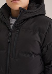 Juodas šiltas džemperis su gobtuvu, turintis lygų išorę, užtrauktuką krūtinės kišenėje ir tekstūruotą vidinį pamušalą.