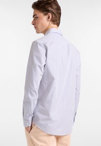 Camisa de manga larga a rayas en azul y blanco, con cuello abotonado y detalles en los puños, hecha de una tela suave con un corte ajustado.
