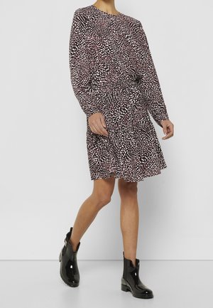 Femme portant une robe à manches longues à motifs noir, blanc et rose avec une taille élastique, associée à des bottines de pluie noires brillantes à la cheville.