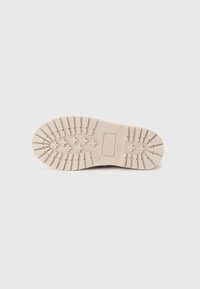 Light beige shoe sole with deep traction grooves, rounded front, and rectangular heel, featuring a textured surface and subtle branding.
