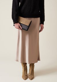 Maglione nero fluffy, gonna satin beige, pochette testurizzata con accento dorato e stivali marroni con stampa serpente a punta.