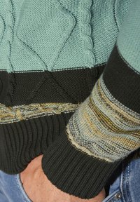 Gestrickter Pullover mit türkisblauen, schwarzen und gestreiften Ärmeln. Verfügt über strukturierte Muster und gerippte Bündchen. Das Material scheint weich und langlebig zu sein.
