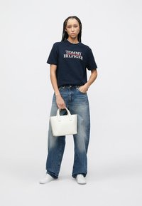 Μπλε βαμβακερό T-shirt με το λογότυπο "TOMMY HILFIGER", άνετο τζιν παντελόνι και μικρό λευκό δερμάτινο τσαντάκι. Υφή υφάσματος και casual σχεδίαση.