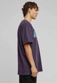 T-shirt en coton violet foncé à manches courtes, arborant un texte graphique coloré sur le devant. Coupe ample et col rond classique.