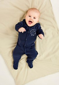 Navyblå bebiskjol med lång ärm och tryckknappar, med en vit elefantgrafik på bröstet, liggande på en beige filt.