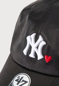 Μαύρο καπέλο με γυαλιστερό φινίρισμα, με λευκό κεντημένο λογότυπο "NY" και μια μικρή κόκκινη καρδιά. Περιλαμβάνει κυκλικό ταμπελάκι "47".