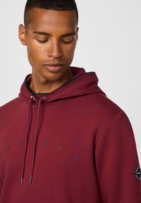 Sudadera burdeos de mezcla de algodón, con capucha ajustable, sutil logotipo en azul oscuro y un acabado de tela texturizada.