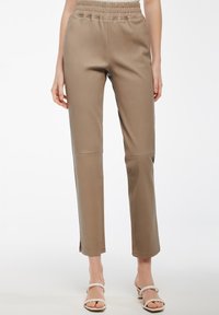 Pantaloni in finta pelle beige con vita alta elastica, gambe taper e spacchi laterali all'orlo. Texture liscia e design slim fit.