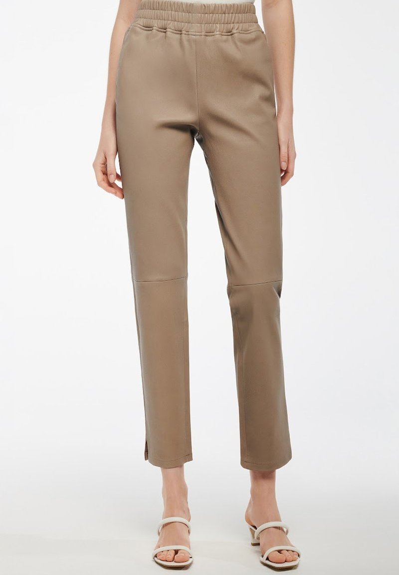 Pantaloni in finta pelle beige con vita alta elastica, gambe taper e spacchi laterali all'orlo. Texture liscia e design slim fit.