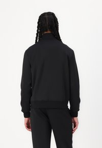 Svart hettetrøye med ribbestrikkede mansjetter og kant, minimalistisk design, myk tekstur og høy krage. Bæres med matchende svarte bukser.