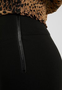 Svarta högmidjade byxor med en sidodragkedjedetalj. Tyget är slätt med en figursydd silhuett. Toppens design har ett leopardmönster.