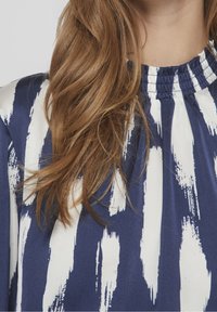 Robe marine avec un motif abstrait de coups de pinceau blancs. Présente un col smocké. Tissu doux, design légèrement structuré, contraste vif.