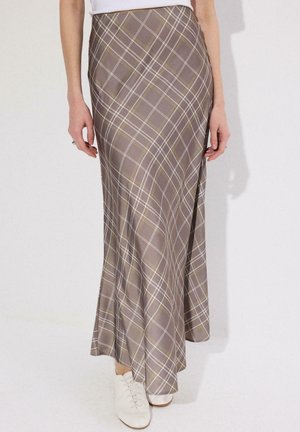 Jupe marron à carreaux taille haute longueur cheville portée avec des chaussures blanches et un haut blanc rentré, montrée de la taille aux pieds.