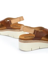 Sandalias de cuero marrón con una correa de marrón claro, plantilla acolchada y suela de plataforma blanca gruesa, con detalles trenzados cerca de la suela.