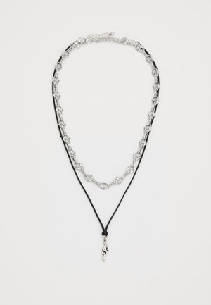 Collana in argento a catena, stratificata con corda nera, con un pendente astratto unico. La catena presenta anelli geometrici; chiusura regolabile.
