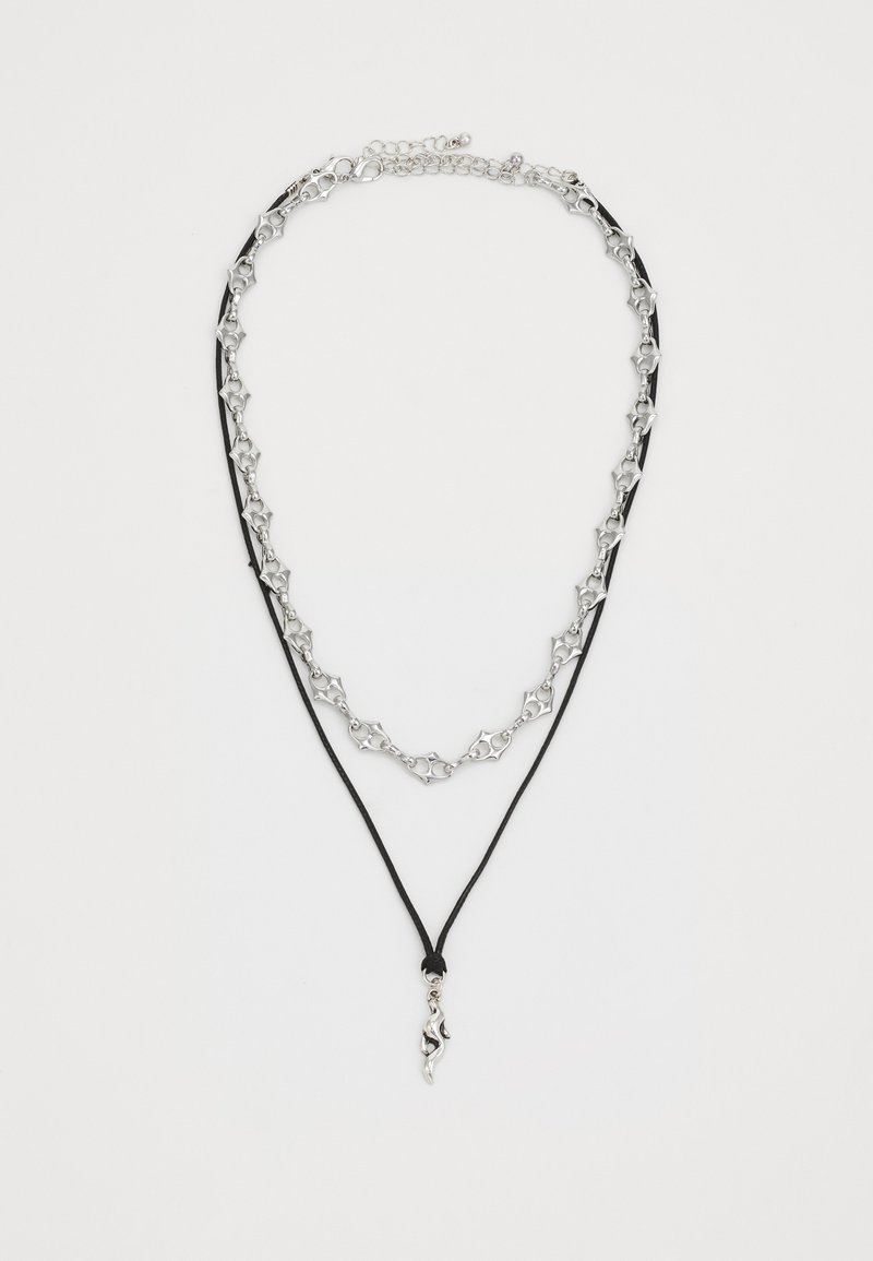 Collana in argento a catena, stratificata con corda nera, con un pendente astratto unico. La catena presenta anelli geometrici; chiusura regolabile.