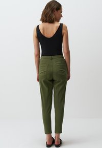 Body nero abbinato a pantaloni verdi oliva strutturati e a vita alta. I pantaloni presentano tasche anteriori e un design a gamba affusolata.