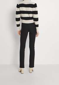 Pull en maille à rayures horizontales noires et crème, associé à un pantalon noir moulant et des chaussures crème à talon bloc. Texture lisse, coupe ajustée.