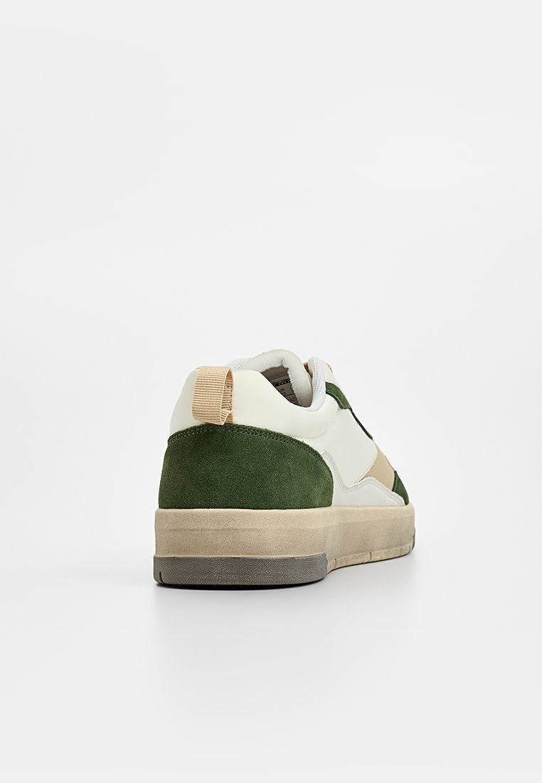 Sneaker in suede verde e pelle bianca con un accento beige, tomaia testurizzata e una suola in gomma morbida, dotata di una linguetta color tan sul tallone.