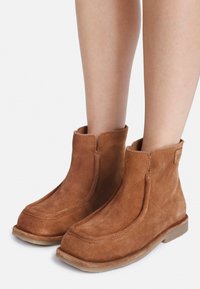 Braune Wildleder-Ankleboots mit glatter Textur, abgerundeter Zehenpartie und einem Slip-On-Design. Mit seitlichen Nähten und einer flachen Sohle.