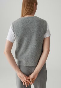 Gilet grigio lavorato a maglia con una texture morbida, indossato sopra una camicia bianca a maniche corte, abbinato a pantaloni grigi su misura. Design semplice, senza fantasie.