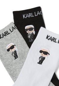 Tři páry ponožek v šedé, černé a bílé. Každé má vyšitou karikaturu postavičky v brýlích, s textem "KARL LAGERFELD" nahoře.