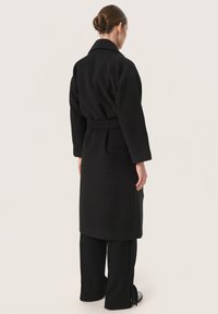 Cappotto in misto lana nero con vita cintata, maniche lunghe e colletto a rever. Il cappotto presenta una silhouette dritta ed è di lunghezza al ginocchio.