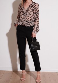 Blusa trasparente con stampa leopardata e rouches sul collo e polsini, abbinata a pantaloni neri a vita alta. Gli accessori includono una piccola borsa nera.
