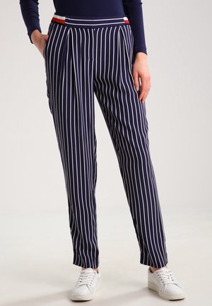 Granatowe spodnie w białe pionowe paski z czerwono-białymi akcentami w talii, noszone z białymi trampkami i granatową bluzką z długim rękawem.