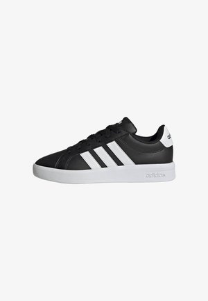 Sneaker Adidas nera low-top con strisce bianche, suola bianca e logo Adidas su tallone e suola intermedia, vista di lato.