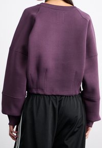 Fialová zkrácená mikina s kulatým výstřihem, spadlými rameny a žebrovanými manžetami; hladká textura s viditelnými švy.