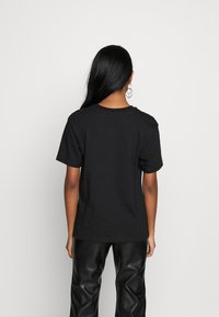 Sort bomulds T-shirt med rund halsudskæring, korte ærmer og en afslappet pasform. Båret med højtaljede, blanke sorte bukser, der har et enkelt design.