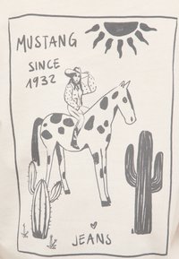 Cowgirl portant un chapeau chevauchant un cheval tacheté entre deux cactus sous le soleil, avec le texte « MUSTANG DEPUIS 1932 » et « JEANS » en dessous.