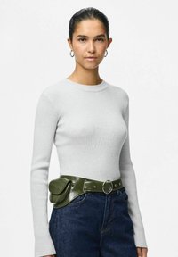 Šedý pruhovaný top s dlouhým rukávem spárovaný se zeleným lesklým páskem s kulatou sponou a kapsičkou, nošený s modrými džínovými kalhotami.