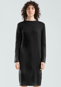 Robe tricotée noire à manches longues, encolure ronde et poignets côtelés. Le tissu a une texture douce et une silhouette droite.