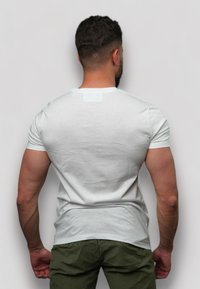T-shirt ajusté blanc à manches courtes, col rond et texture lisse, porté avec un pantalon vert olive, vu de dos.