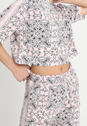 Personne portant un haut court rose pâle à motif cachemire et un pantalon à cordon assorti avec des bandes latérales, laissant entrevoir le ventre.