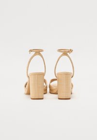 Sandales à talons carrés beiges avec un dessus en tissu texturé, une sangle autour de la cheville et une ouverture au niveau des orteils, dotées d'un design de talon carré robuste.