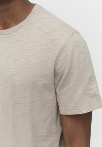 Lys beige kortærmet t-shirt lavet af et struktureret stof med en glat finish, der har en klassisk rund halsudskæring og subtile farvevariationer.