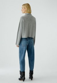 Grijze cropped sweater met lange mouwen, gecombineerd met hoge jeans in een blauwe kleur. Draagt met zwarte enkellaarsjes, die een ontspannen pasvorm laten zien.
