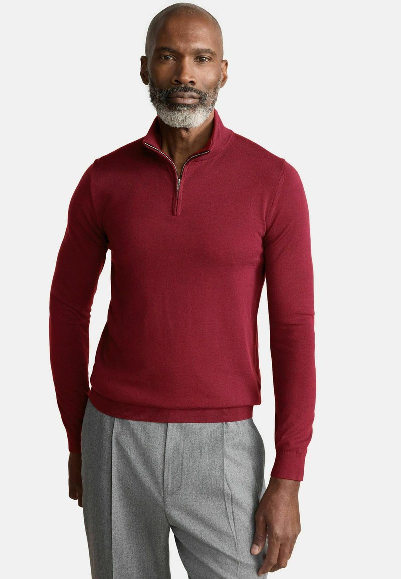 Pulover tricotat color burgund cu guler cu fermoar pe un sfert, mâneci lungi, design ajustat și tiv cu riburi, asortat cu pantaloni călcați de culoare gri deschis.