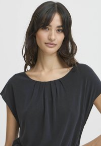 Schwarzes T-Shirt mit kurzen Ärmeln und rundem Ausschnitt, das vorne kleine Falten aufweist. Der Stoff sieht weich aus und hat einen leichten Glanz.