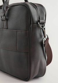 Bolso de cuero texturizado marrón con cierre de cremallera, que presenta un bolsillo lateral, correa ajustable y acentos de metal.
