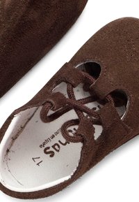 Scarpa in suede marrone con chiusura con lacci, presenta dettagli tagliati, punta arrotondata e una soletta bianca con dettagli del brand stampati.