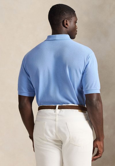 Ανοιχτό μπλε πόλο πουκάμισο με κοντά μανίκια, υφασμάτινη υφή και κλασικό γιακά, σε συνδυασμό με λευκό παντελόνι και καφέ ζώνη.