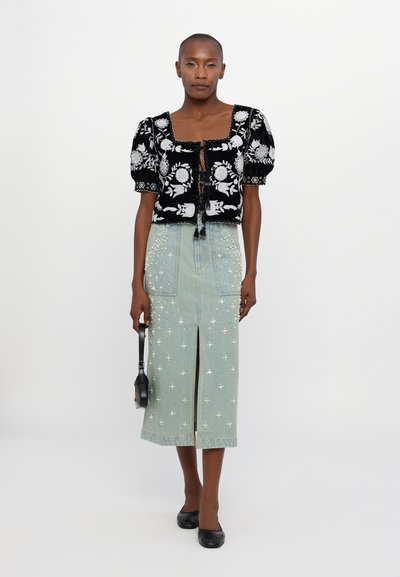 Μαύρη κεντημένη κοντή μπλούζα με φουσκωτά μανίκια, συνδυασμένη με μια ανοιχτό μπλε τζιν φούστα με λουλουδάτα στολίσματα και μπροστινό σκίσιμο.