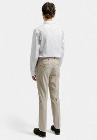 Vitt skjorta med en strukturerad krage, ljusbeiga skräddarsydda byxor och bruna skor, sedd bakifrån som visar en ren design.