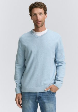 Lichtblauwe v-hals trui van zacht materiaal, met lange mouwen en geribbelde zoom. Draagt over een witte ronde hals t-shirt. Casual uitstraling.
