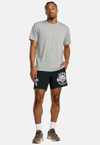 Gray t-shirt, black shorts with white graphic design, and brown sneakers. The outfit features a relaxed fit and contrasting colors.