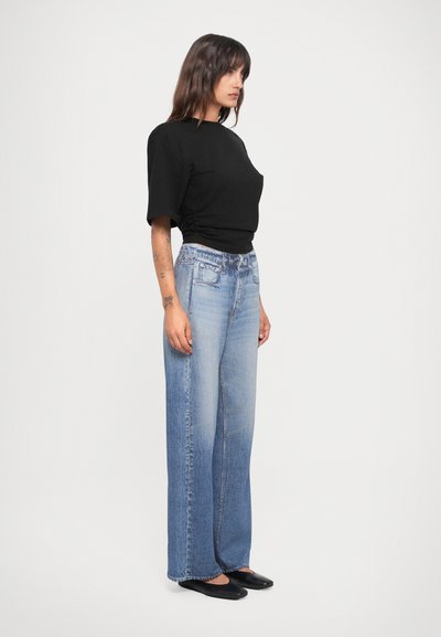 Svart topp med kort erm kombinert med lyseblå, vide denimjeans med falmet effekt. Modellen har på seg svarte flate sko.